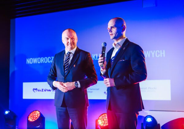 Dwóch mężczyzn w garniturach stoi na scenie podczas prezentacji powiatowej młodzieżowej kadry piłki nożnej w powiecie płockim.