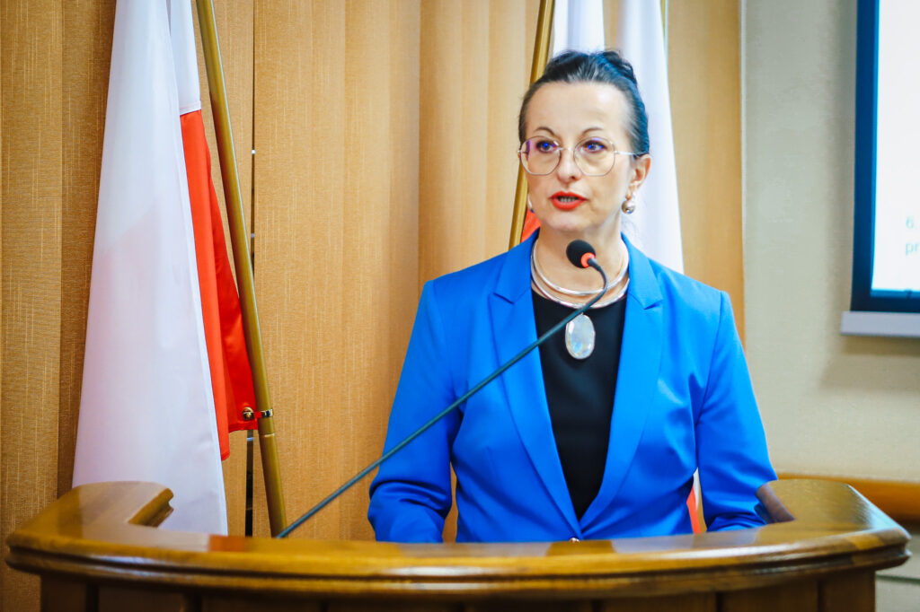 Kobieta w niebieskim żakiecie wygłasza przemowę z mównicy podczas XIX sesji Rady Powiatu Płockiego w kadencji 2024–2029.