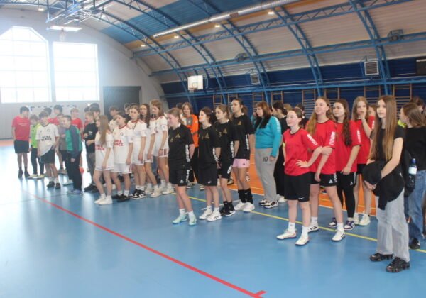 Grupa młodych zawodniczek i zawodników stoi w rzędzie na boisku hali podczas powiatowych finałów w halowej piłce nożnej.