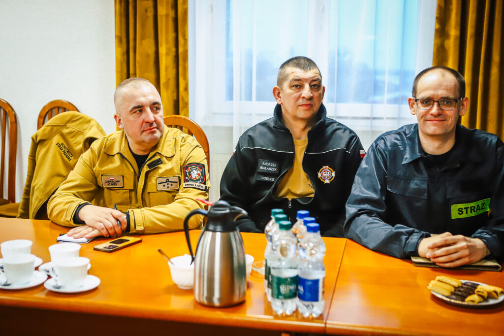 Trzech strażaków ochotników siedzi przy stole w sali konferencyjnej podczas spotkania z przedstawicielami Fundacji ORLEN.