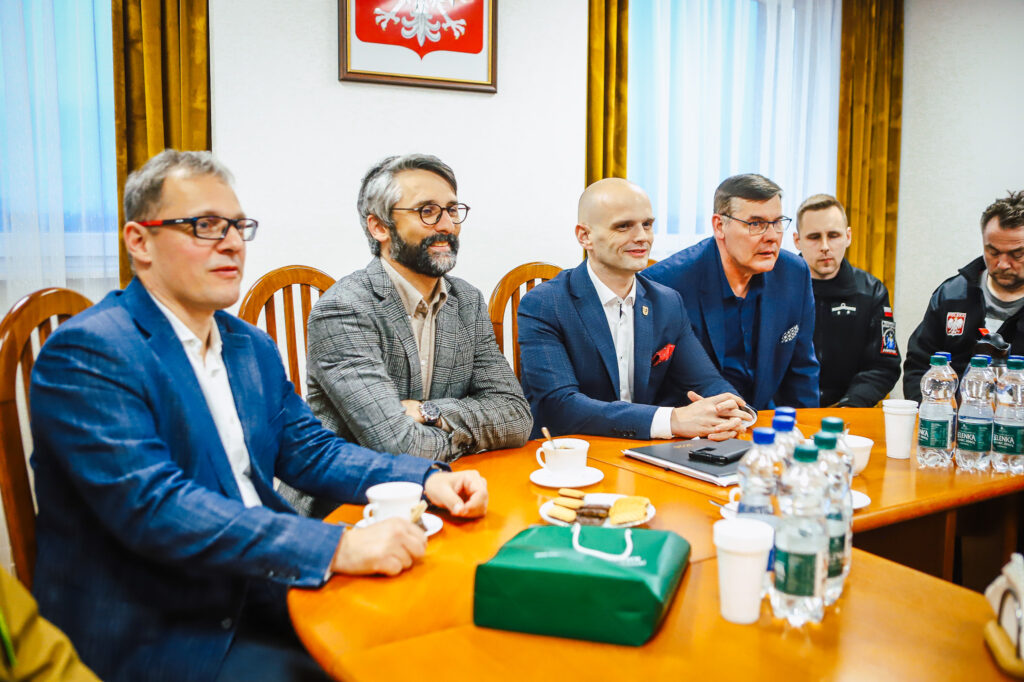 Grupa strażaków ochotników i przedstawicieli Fundacji ORLEN siedzi przy długim stole w sali konferencyjnej podczas spotkania, z napojami i przekąskami na stole.