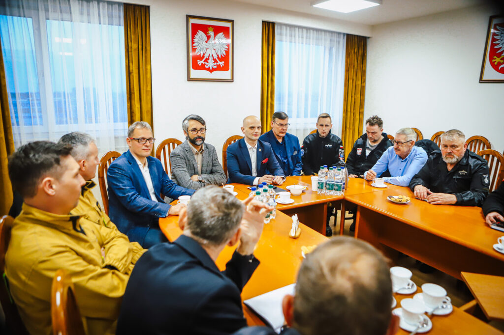 Grupa strażaków ochotników i przedstawicieli Fundacji ORLEN siedzi przy stole w sali konferencyjnej i prowadzi rozmowę podczas spotkania.