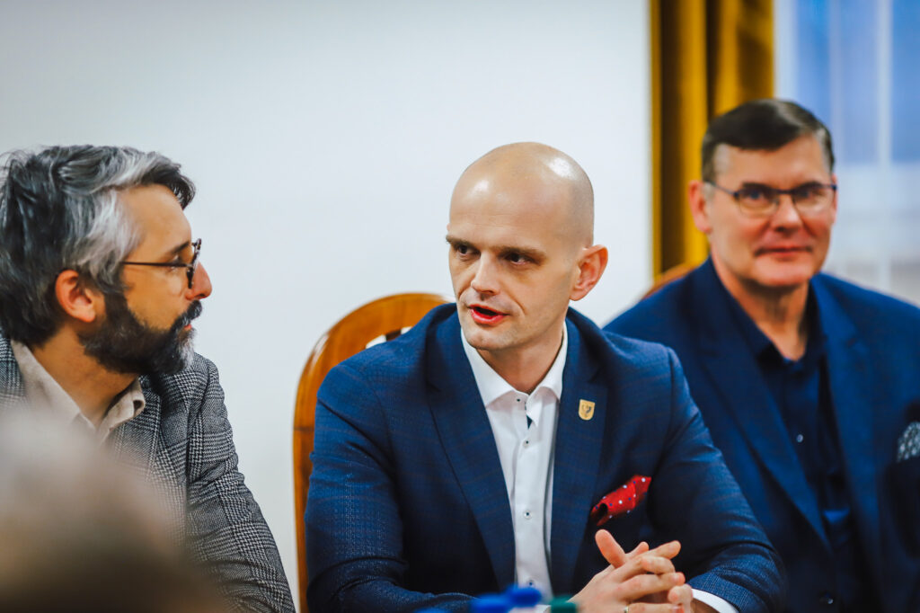 Trzech mężczyzn w garniturach siedzi przy stole podczas spotkania strażaków ochotników z przedstawicielami Fundacji ORLEN.