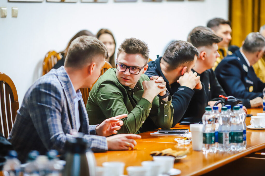 Grupa strażaków ochotników rozmawia przy długim stole w sali konferencyjnej podczas spotkania z przedstawicielami Fundacji ORLEN.