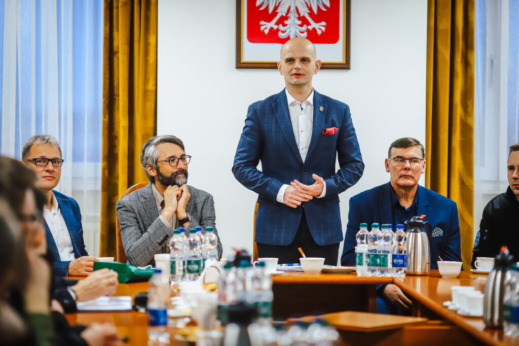 Mężczyzna w granatowym garniturze przemawia stojąc przy stole podczas spotkania strażaków ochotników z przedstawicielami Fundacji ORLEN w sali konferencyjnej.