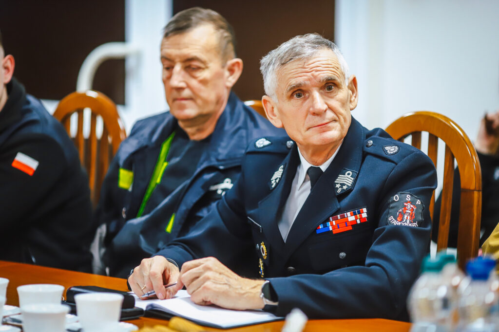 Strażak ochotnik w mundurze z odznaczeniami siedzi przy stole podczas spotkania z przedstawicielami Fundacji ORLEN.