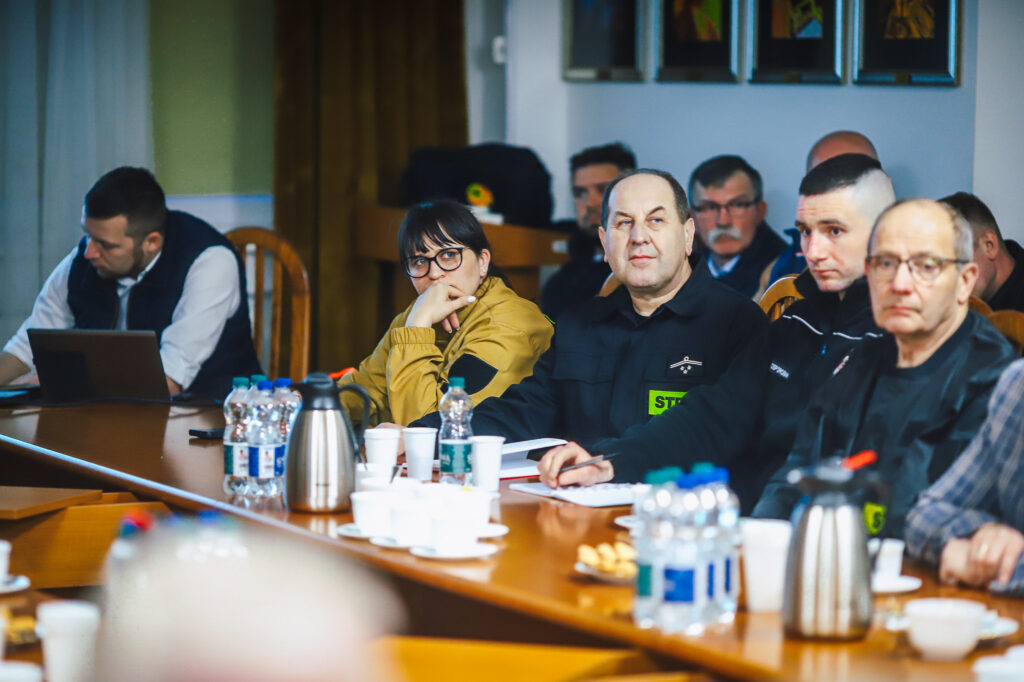 Grupa strażaków ochotników i przedstawicieli Fundacji ORLEN siedzi przy stole w sali konferencyjnej podczas spotkania.