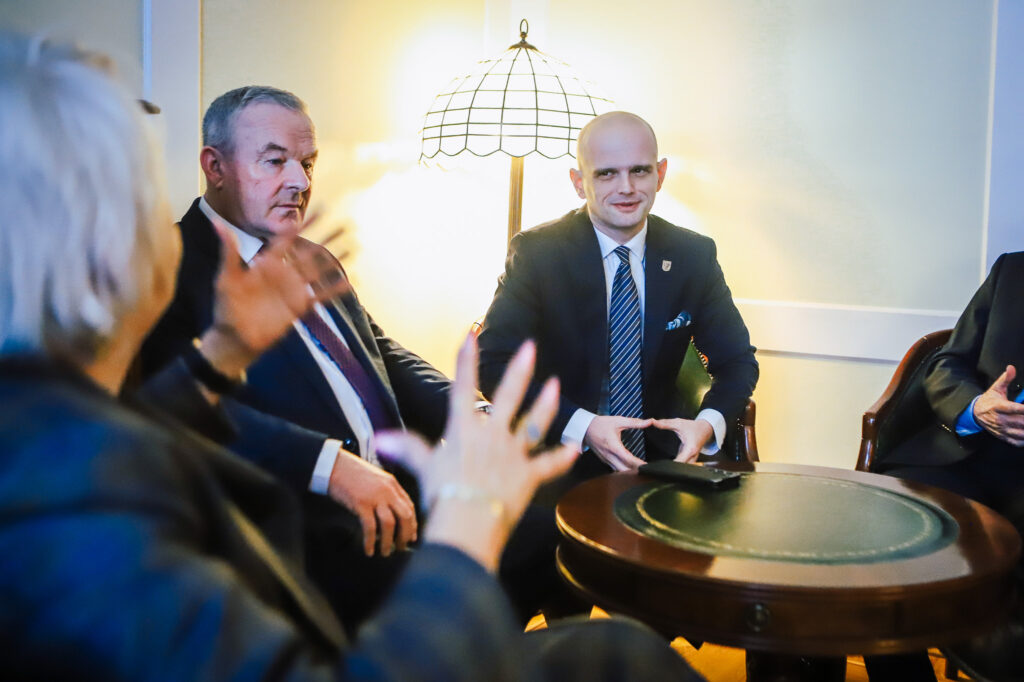 Dwóch mężczyzn w garniturach siedzi przy okrągłym stole podczas spotkania w biurze, omawiając przebieg trasy S10 w pobliżu Płocka.