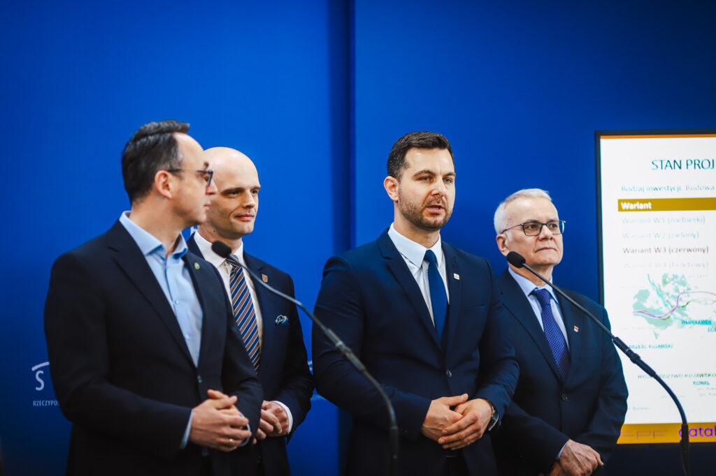 Czterech mężczyzn w garniturach podczas konferencji prasowej dotyczącej przebiegu trasy S10 w pobliżu Płocka.