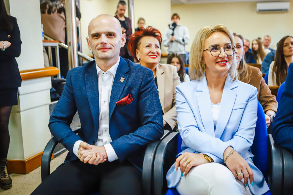 Mężczyzna i kobieta w eleganckich marynarkach siedzą na krzesłach podczas uroczystego podsumowania Finału WOŚP w powiecie płockim.