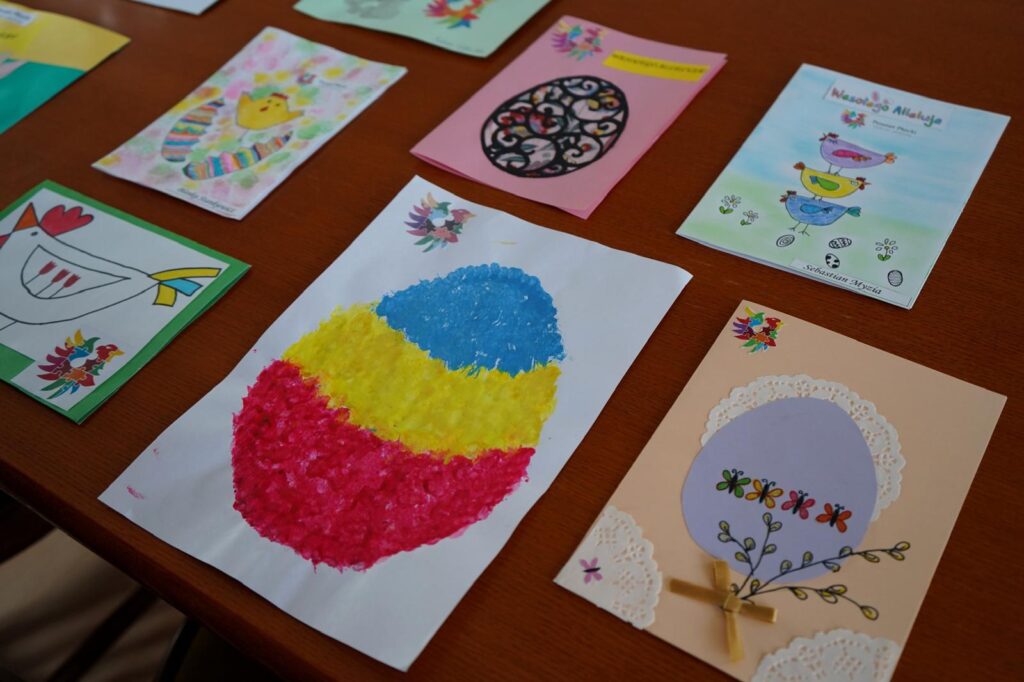 Na tle drewnianego stołu leżą kolorowe, ręcznie wykonane kartki wielkanocne z konkursu Powiatu Płockiego.