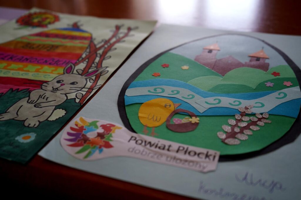 Kolorowe kartki wielkanocne na konkurs Powiatu Płockiego: z lewej rysunek zajączka na tle tęczowych pasków, z prawej okrągła kompozycja z krajobrazem rzeki, wzgórz i zamków.
