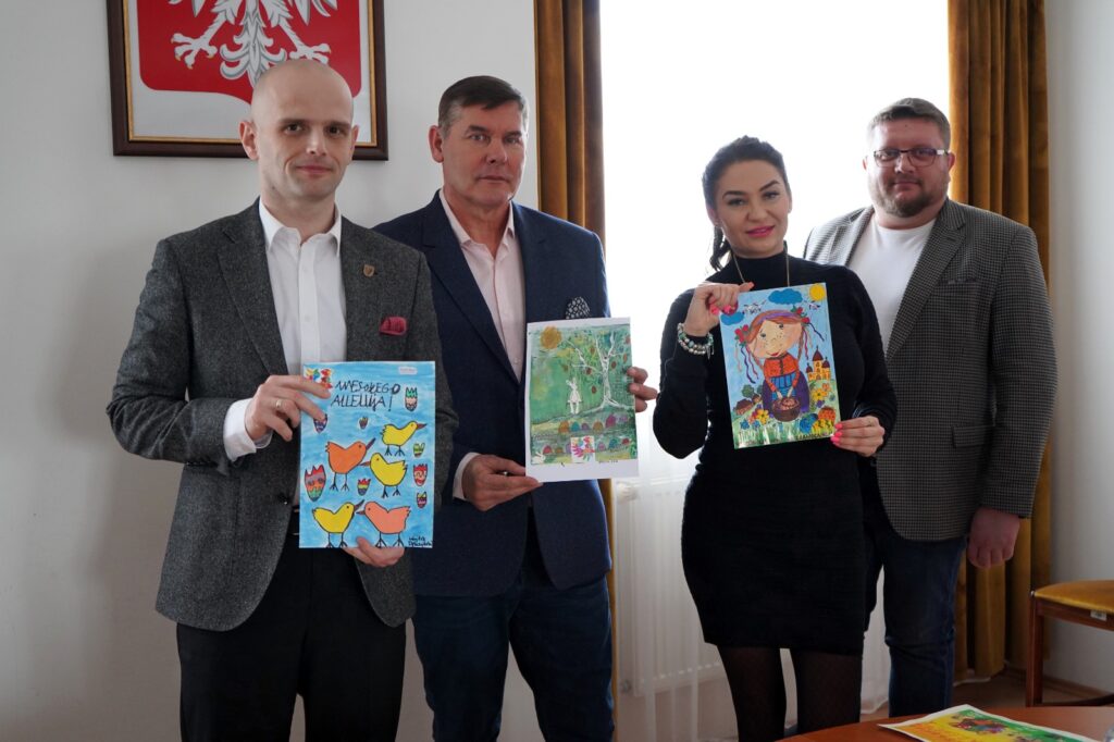 Cztery osoby stoją w biurze i prezentują kartki wielkanocne wyłonione w konkursie Powiatu Płockiego.