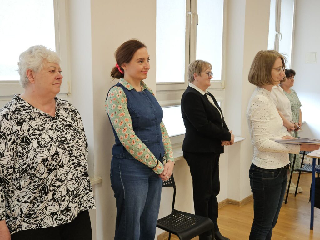 Grupa kobiet stoi w rzędzie w jasnym pomieszczeniu podczas zakończenia kwalifikacji wojskowej w Powiecie Płockim.