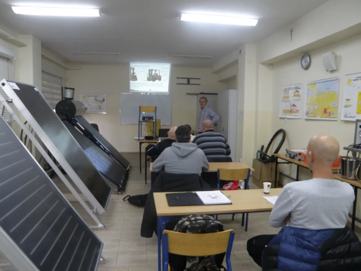 Uczestnicy kursu zawodowego dla osób niepełnosprawnych w powiecie płockim siedzą w sali szkoleniowej i oglądają prezentację na projektorze, obok ustawione są panele słoneczne.